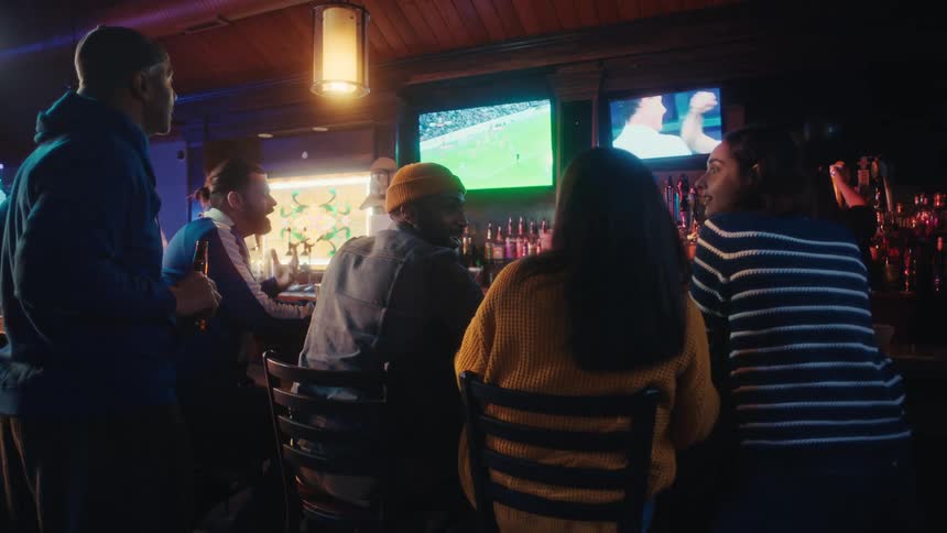 Group of people gathered in a bar watching a sports match on televisions above the counter