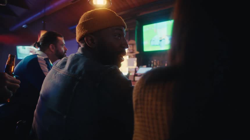 The people in the bar cheer while watching a sports game on the tv