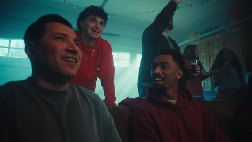 Group of friends talking and laughing while having drinks and watching something on a screen indoors during day time