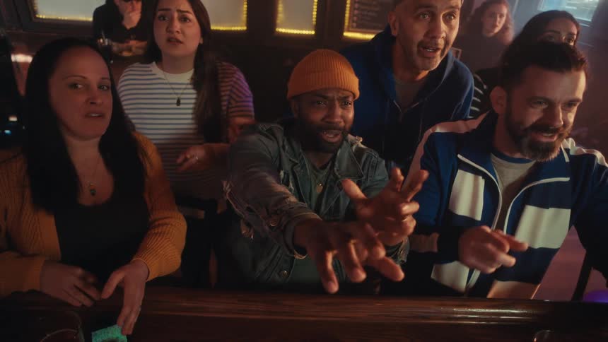 A group of friends cheers and reacts with excitement while watching a match at a lively bar at night