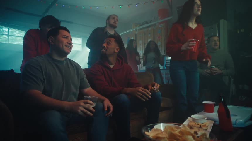 Group of people gathered in a living room seated and standing with drinks and food during a social gathering