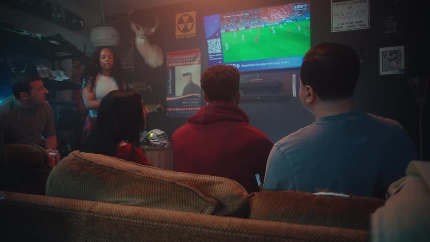 Group of people seated indoors watching a sports match displayed on a television