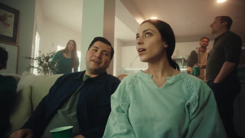 The video shows a group of friends gathered in a living room focused intensely on a screen that is offcamera their expressions shift from quiet anticipation to excitement and smiles as they react to what they are watching