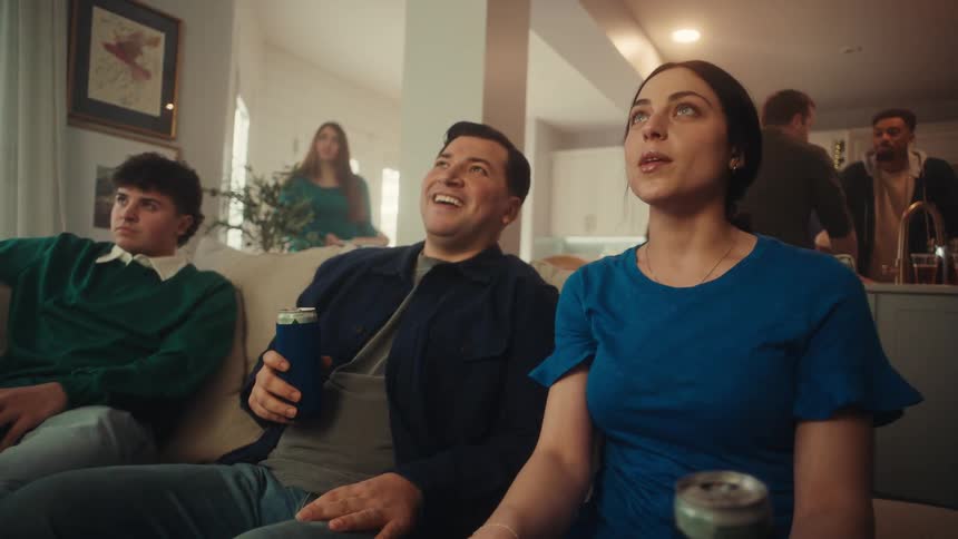 People seated on a couch watching something offscreen during a social gathering in a home setting