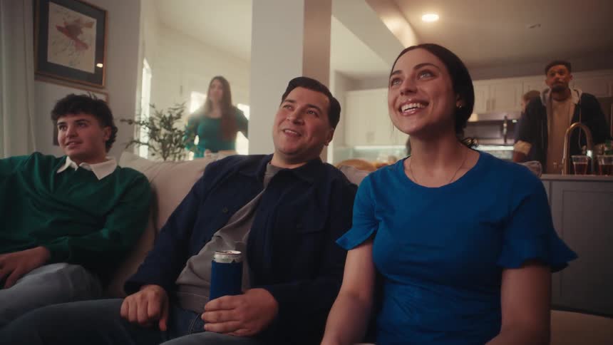 A group of friends laughs together while lounging on a couch at a indoor house party