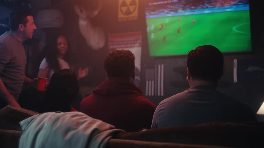A diverse group of friends watching a soccer match on a large television screen in a bar