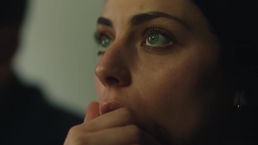 Female face in closeup with hand near the mouth and gaze fixed offscreen