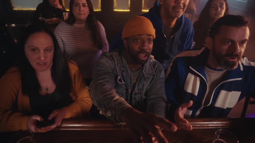 People gathered in a bar celebrating and reacting to an offscreen broadcast at the counter