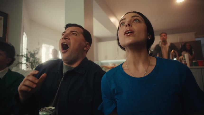 People seated on a couch watching something offscreen in a home setting during a social gathering