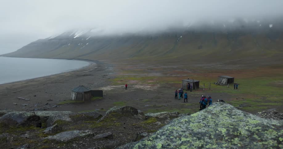 Coastal area with simple structures a group of people and fogcovered mountains in the background