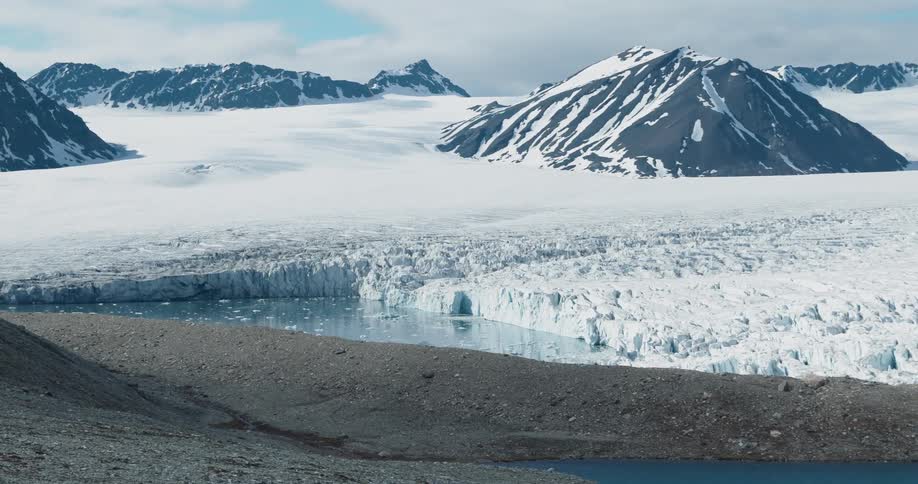 A vast glacier stretches across a frozen valley beneath snow covered mountains in an wide arctic landscape