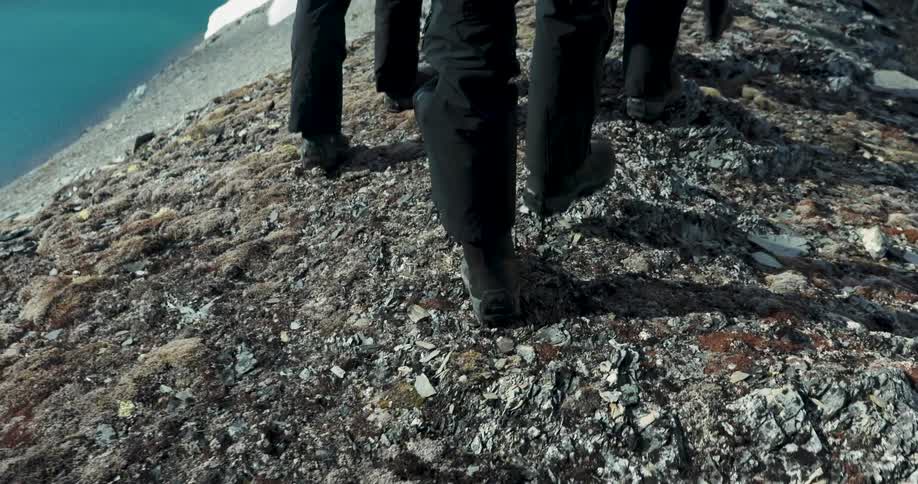 People walk across rocky terrain near a body of water in a natural environment