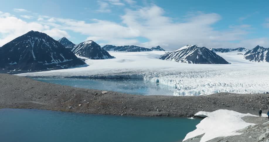 A vast glacier stretches between rugged snow covered mountains beside a calm blue lake