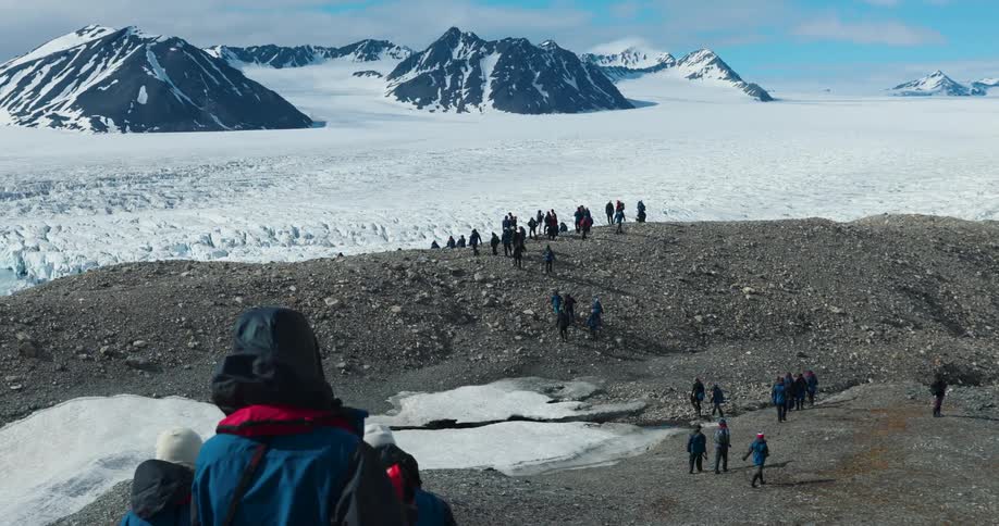 People walk across earthen hills to stand looking at snowy terrain dotted with mountains on a winter day