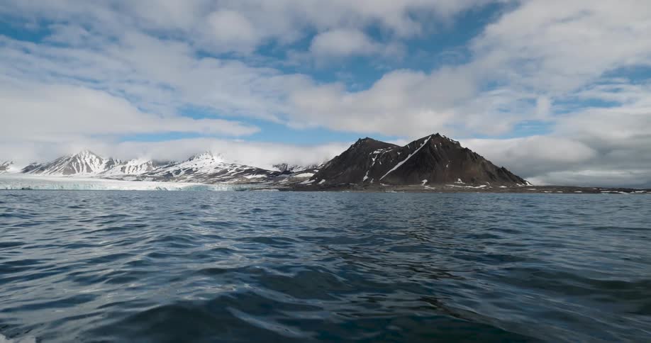 A boat moving toward the shoreline at midday with a snowcovered mountain range along the coast