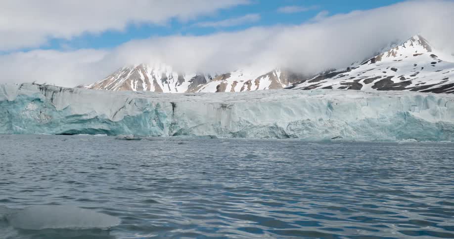 Extensive glacier beside the sea with snowcovered mountains partially shrouded by clouds in the background