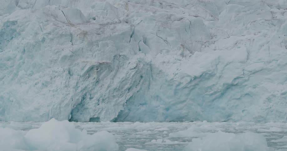 Ice wall with bluish layers above cold water with floating fragments
