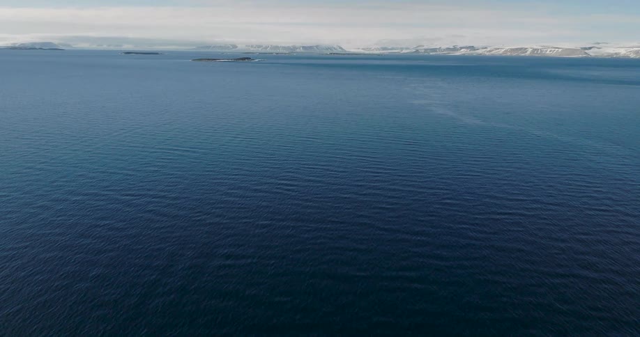 Blue ocean expanse with scattered islands and an icecovered coastline on the horizon under a clear sky