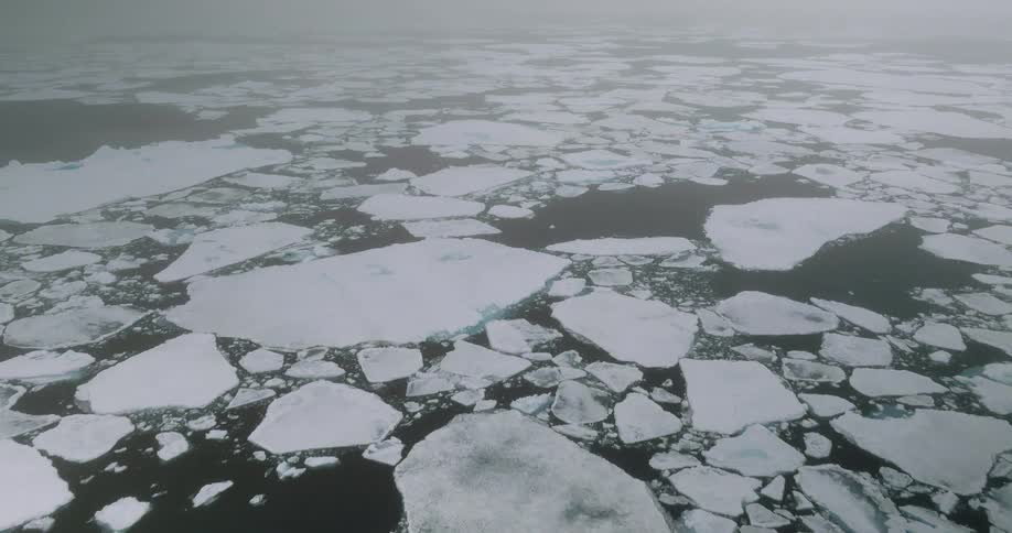 Aerial view of broken sea ice floes drifting across a vast foggy arctic ocean landscape