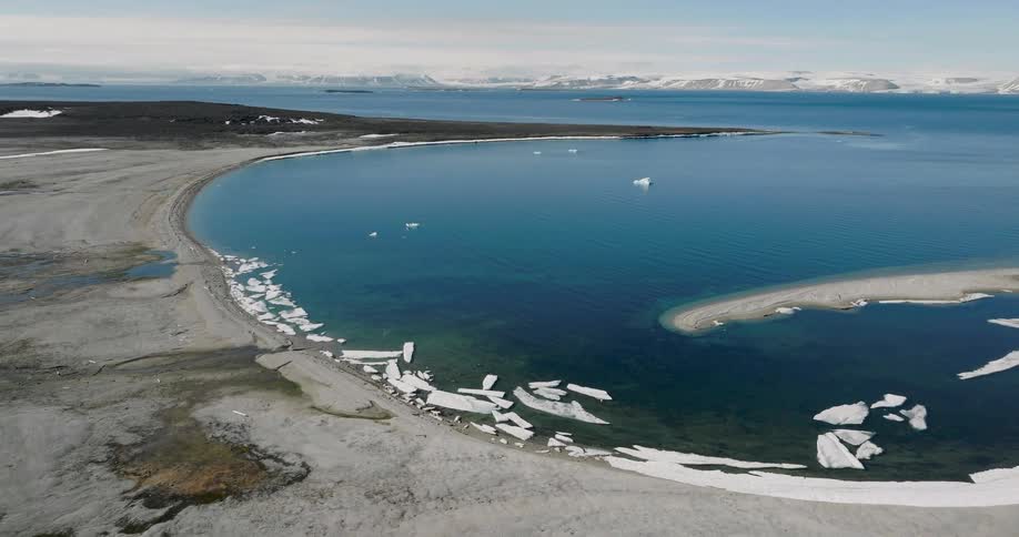 Large pieces of ice floating along the coast with snow covered mountains in the distance