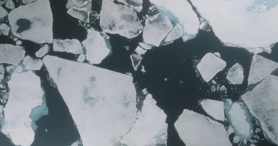 Aerial view of fractured ice floes drifting across the dark surface of arctic waters