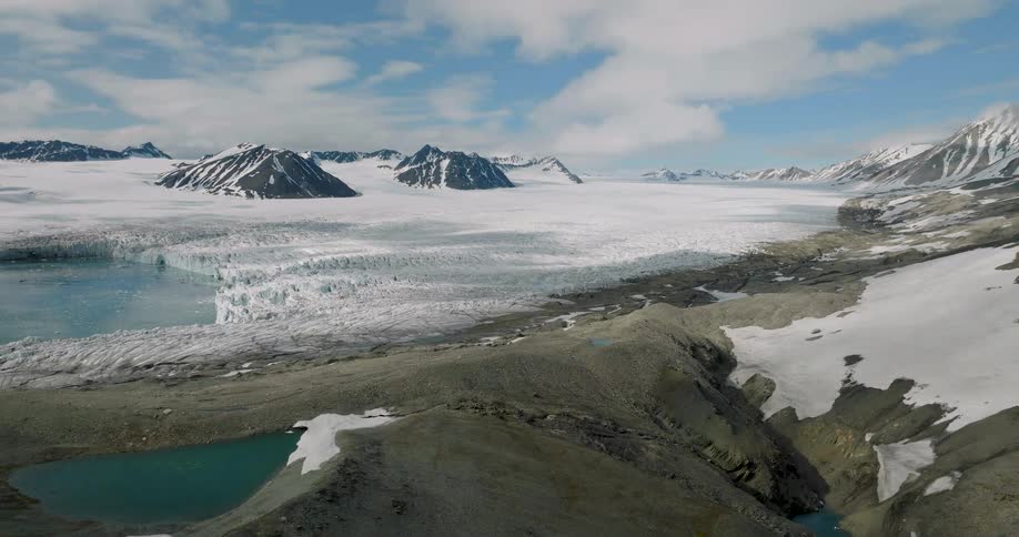 Arctic glacier stretches between rugged mountains with meltwater pools beneath a bright sky