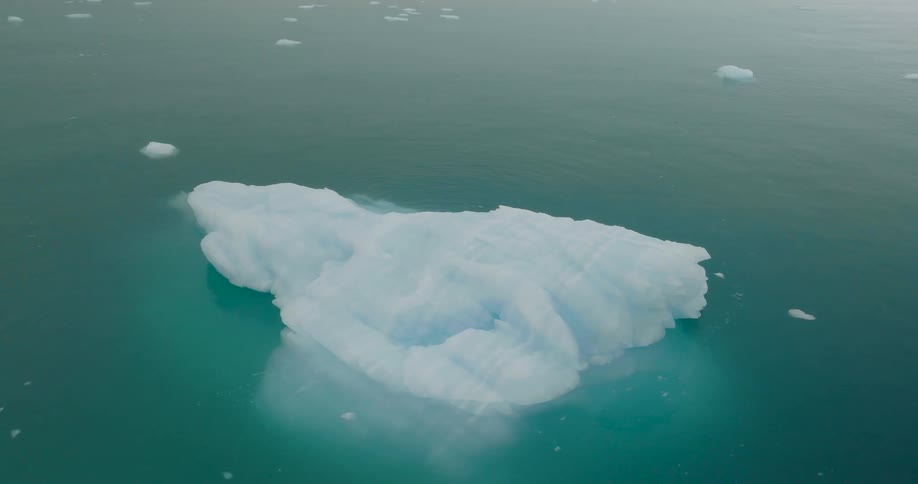 An aerial view of a white iceberg floating in the blue arctic waters