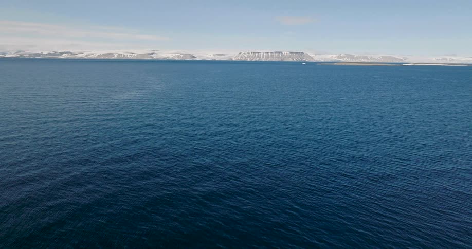 Blue ocean expanse with an icy coastline and snowcovered formations on the horizon under a clear sky