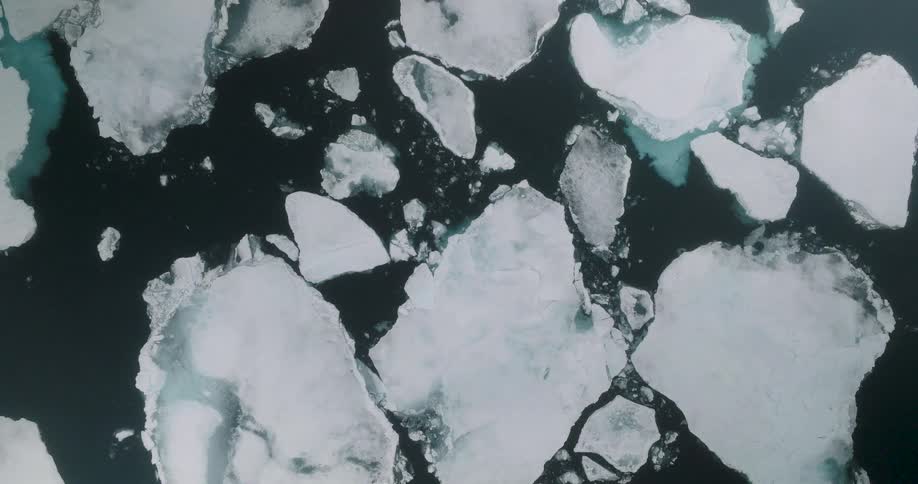 Aerial footage shows large jagged ice floes drifting slowly across a dark calm ocean the highangle shot highlights the stark contrast between the white ice and the deep blue water