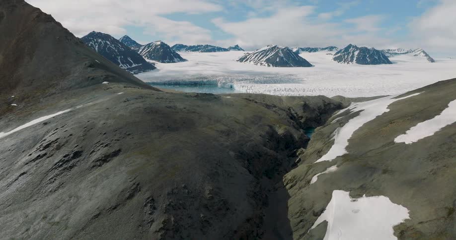 A mountain range with snowcovered peaks and beyond it a lake frozen solid under a layer of ice and snow at midday