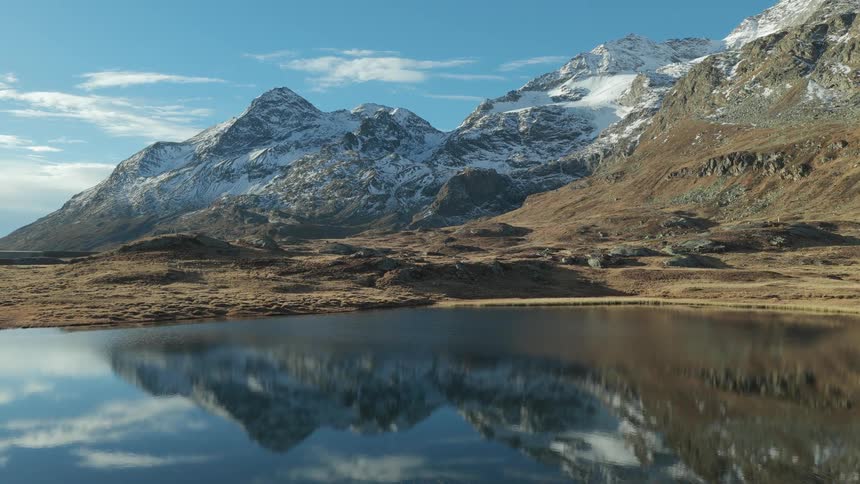 Snowcovered mountains reflect in a calm lake under a clear blue sky
