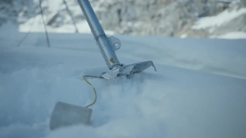 A close view shows a metal tool attached to a yellow wire being pulled through deep snow