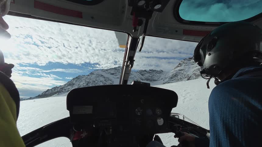 Pilot and his passenger fly over the snow covered terrain leading to the snowy mountains on a cloudy winter day