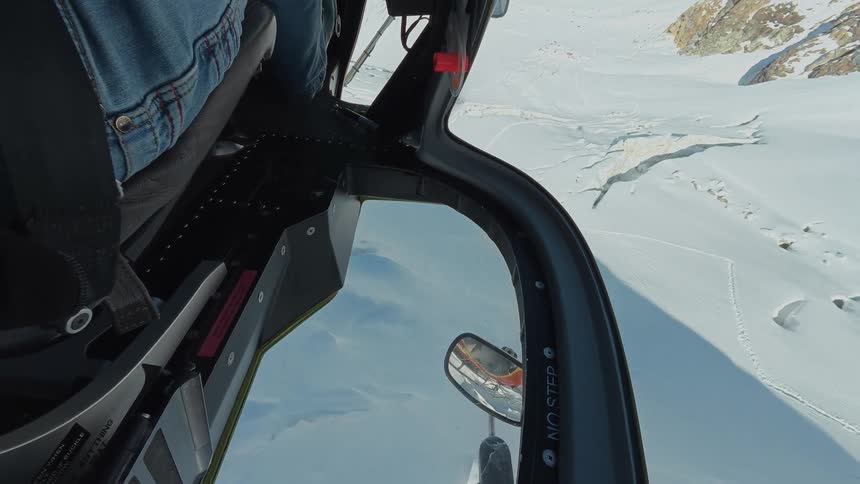 Helicopter piloted over snowy mountainous terrain on a winter day casts a shadow on the snow
