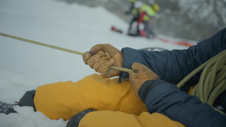 Man on a snow covered mountain holds a rope with other men in the distance