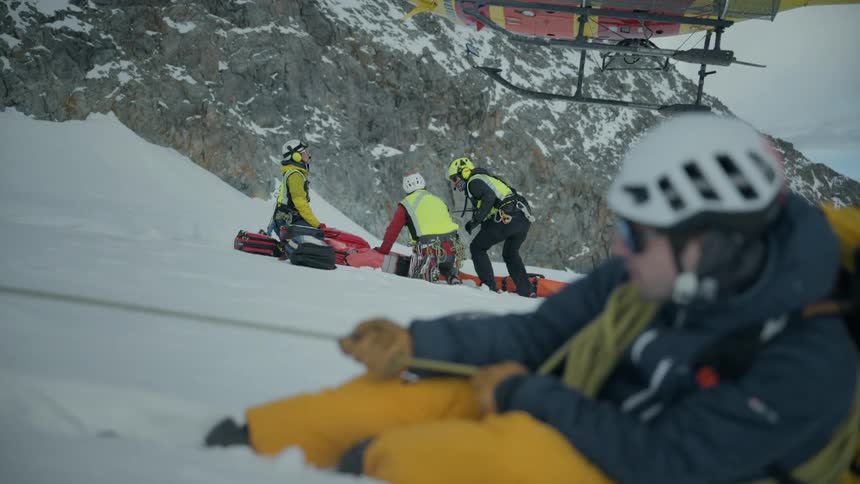 Rescue team prepares an evacuation on a snowy slope beside a yellow helicopter