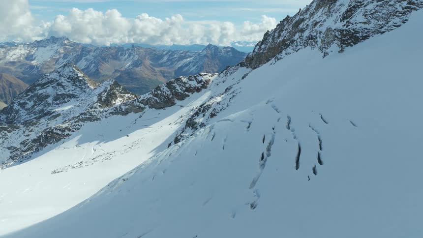 Snowcovered alpine slope with rugged mountain ranges in the background under a partly cloudy sky