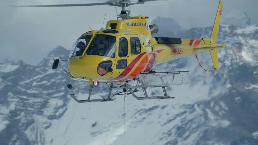 The helicopter is flying with a rope hanging over the mountains