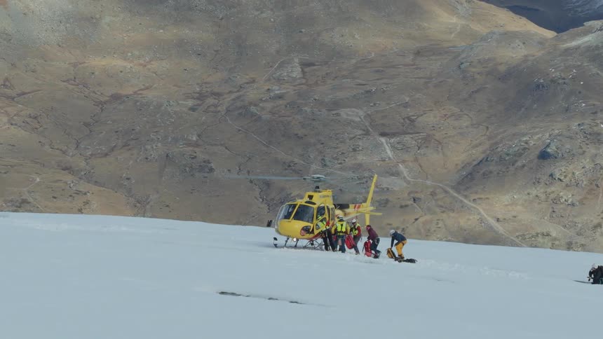 Rescue team assists an injured person on a snowy slope beside a yellow helicopter