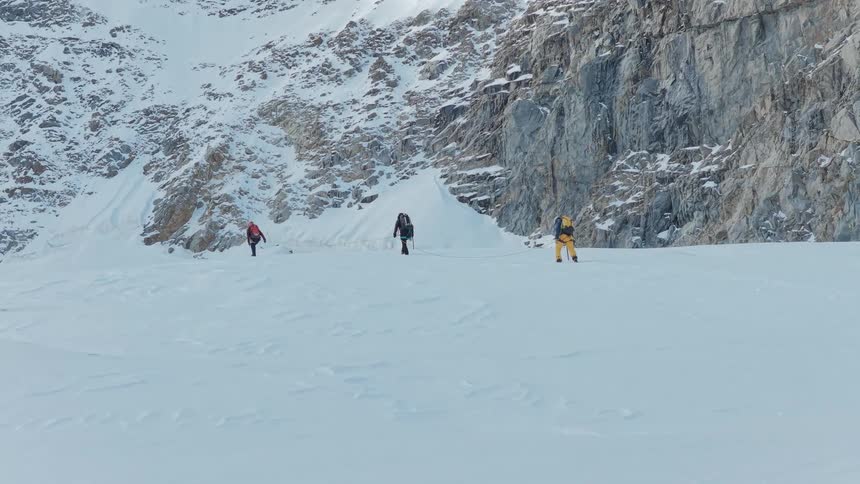 Group of mountaineers crossing a snowy area at the base of a rocky cliff
