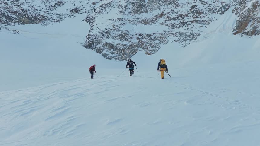 Three men hold a rope and poles as they walk down a snow covered mountain slope