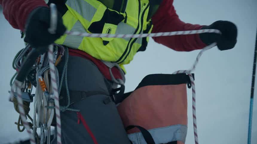 Mountain climber organizes his rope while standing on the snow on a winter day