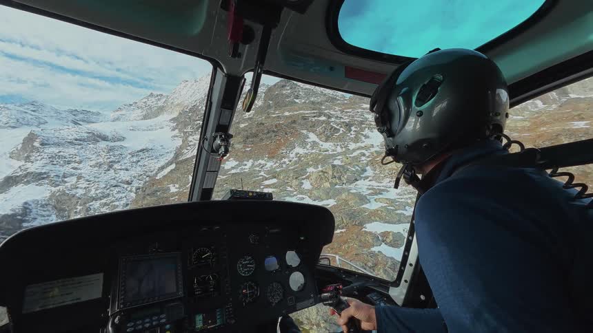 Male pilot steers a helicopter over snowy mountainous terrain on a winter day