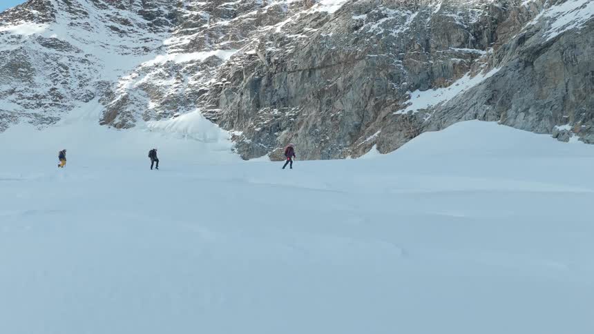 Three men hiking in snow covered mountains holding poles as they walk