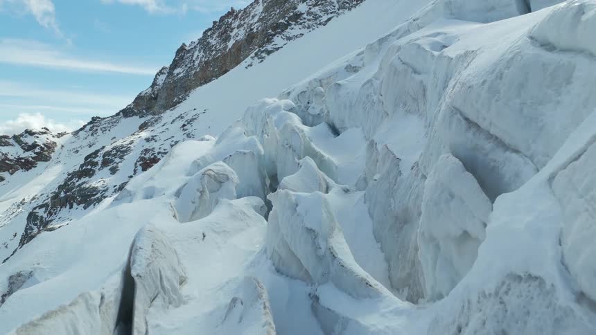 A close aerial view shows the jagged and uneven surface of a massive white glacier with deep cracks and ice formations