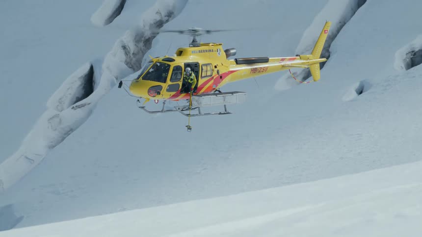 Rescue helicopter hovers above a glacier with a crew member operating external equipment to find trapped people in a crevasse