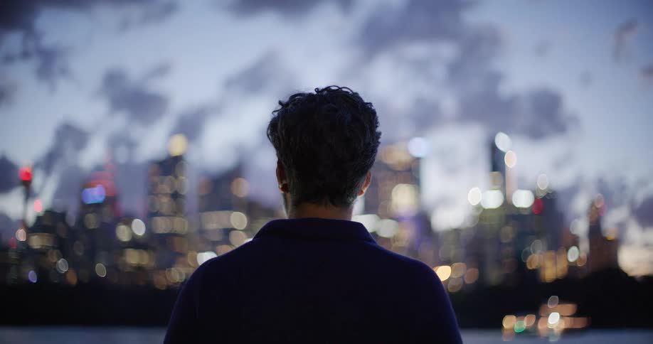 Person seen from behind facing an illuminated city skyline at dusk