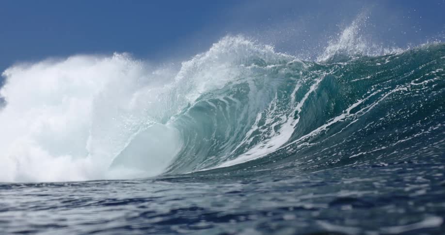 A massive turquoise wave curls into a powerful barrel its crest spraying white mist into the clear blue skythe churning water creates intricate white foam patterns along the face of the wave as it crashes forward