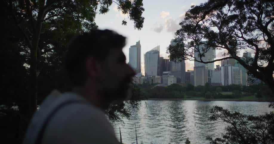 Man sitting along the coast looking at downtown buildings across the river