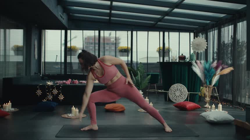 A woman wearing glasses sits on a couch while drinking tea and talking to another person in the other videos she transitions through various yoga poses including stretching upward into a seated meditative position and performing a side angle stretch on